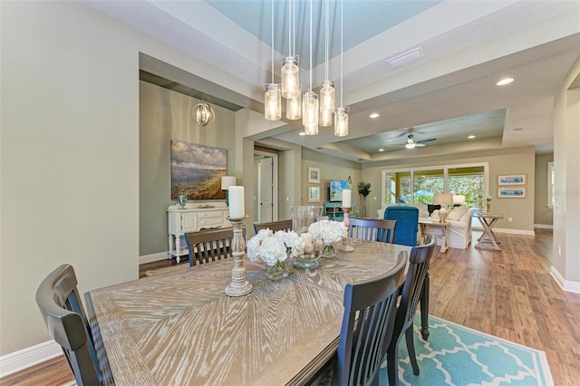 dining room with a tray ceiling, hardwood / wood-style floors, and ceiling fan with notable chandelier