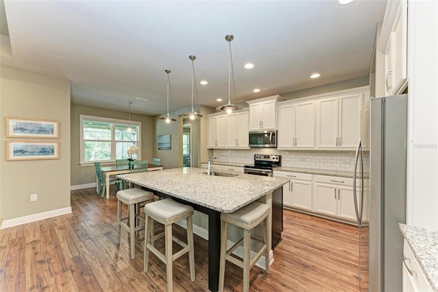 kitchen featuring pendant lighting, a center island with sink, a kitchen breakfast bar, light stone countertops, and stainless steel appliances