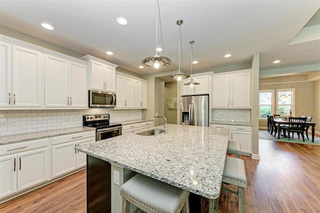 kitchen with pendant lighting, a center island with sink, a kitchen breakfast bar, white cabinetry, and stainless steel appliances