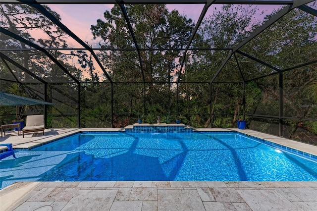 pool at dusk with pool water feature, a lanai, and a patio