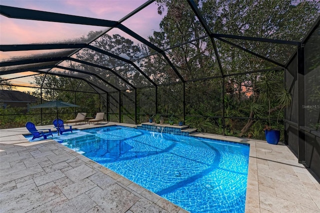 pool at dusk featuring pool water feature, glass enclosure, and a patio area