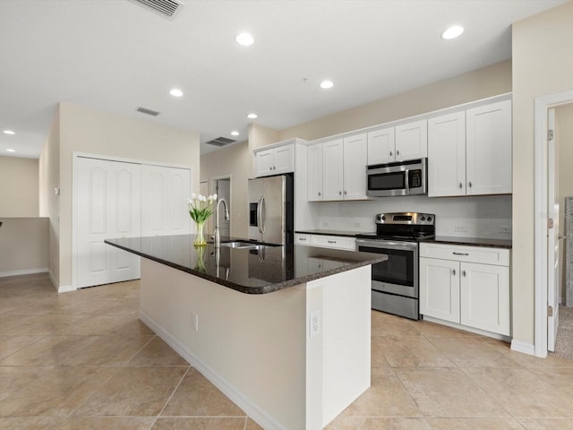 kitchen with appliances with stainless steel finishes, sink, a center island with sink, dark stone countertops, and white cabinetry