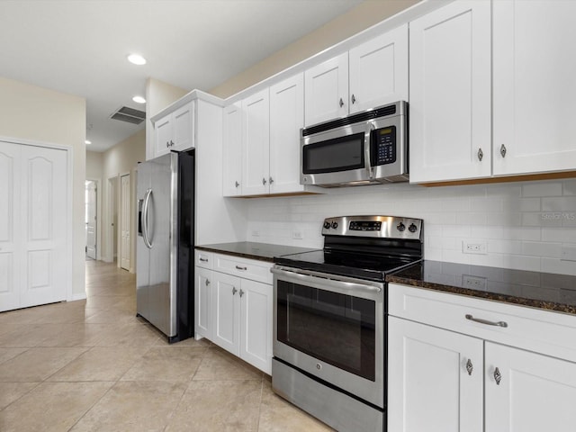 kitchen with dark stone counters, white cabinets, stainless steel appliances, and light tile patterned floors