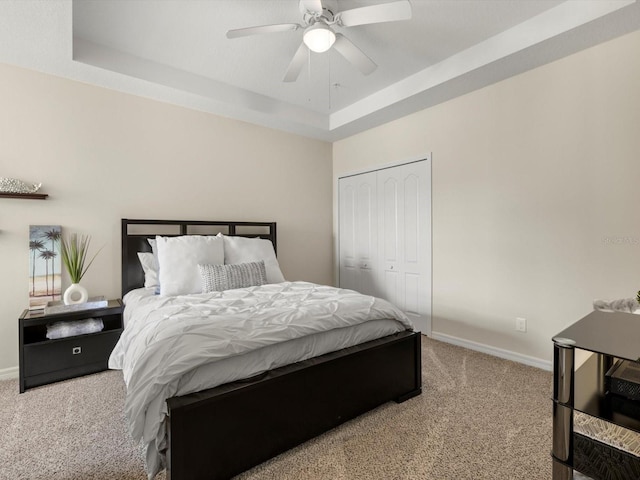 carpeted bedroom featuring ceiling fan, a tray ceiling, and a closet