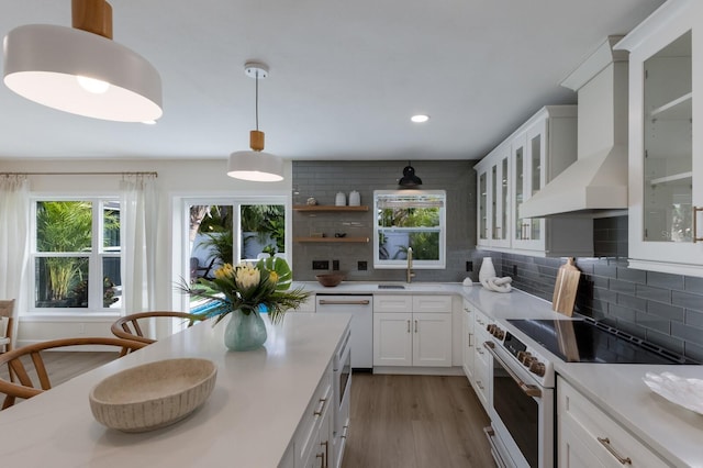 kitchen featuring decorative backsplash, high end stove, wall chimney range hood, dishwasher, and white cabinets