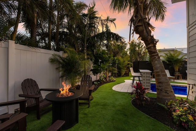 yard at dusk with a fenced in pool, a patio area, and a fire pit