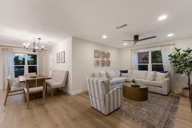 living room featuring ceiling fan with notable chandelier and light wood-type flooring