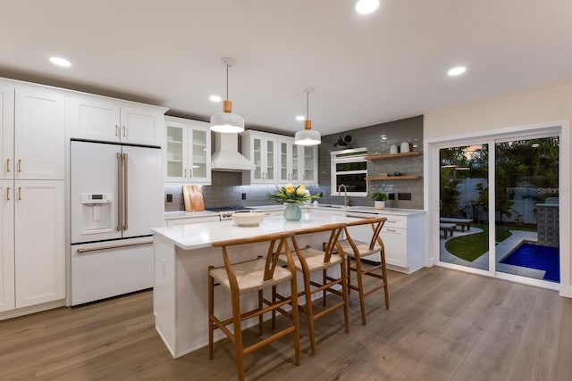 kitchen with pendant lighting, sink, custom range hood, high end fridge, and white cabinetry