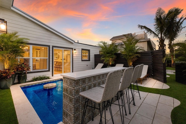 pool at dusk with a patio area and a bar