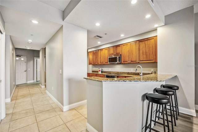 kitchen featuring light stone countertops, light tile patterned floors, kitchen peninsula, and a breakfast bar area