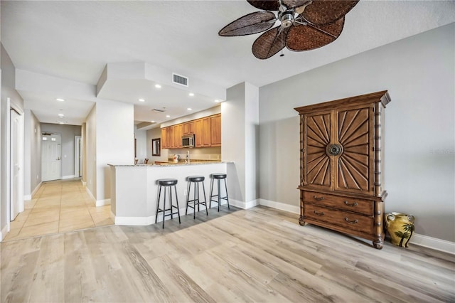 kitchen with sink, ceiling fan, light hardwood / wood-style floors, kitchen peninsula, and a breakfast bar area