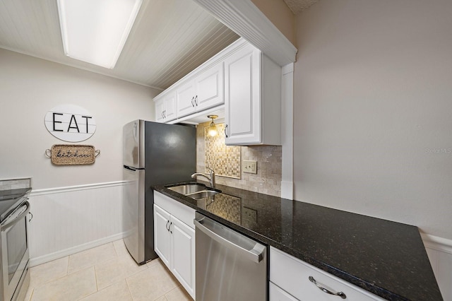 kitchen with stainless steel appliances, dark stone countertops, white cabinetry, light tile patterned flooring, and sink