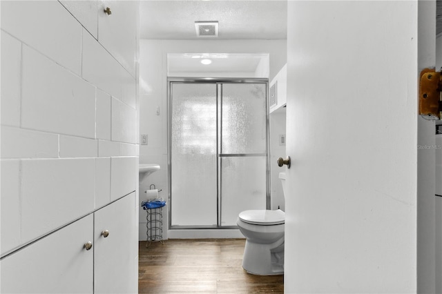 bathroom featuring hardwood / wood-style flooring, toilet, and a shower with shower door