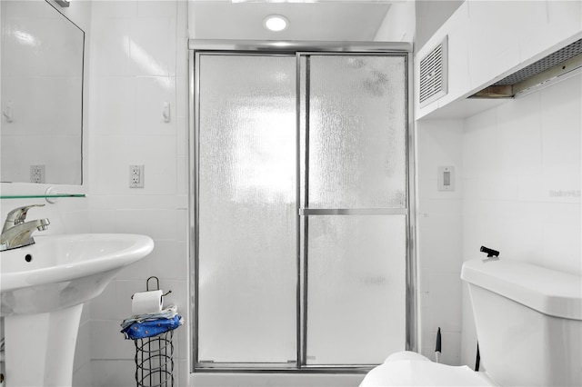 bathroom featuring sink, a shower with shower door, tile walls, and toilet