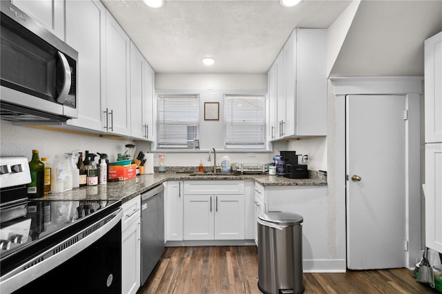 kitchen featuring white cabinetry, sink, stainless steel appliances, dark hardwood / wood-style flooring, and dark stone countertops