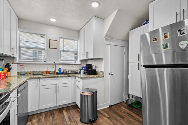 kitchen featuring appliances with stainless steel finishes, dark stone counters, sink, white cabinets, and dark hardwood / wood-style floors