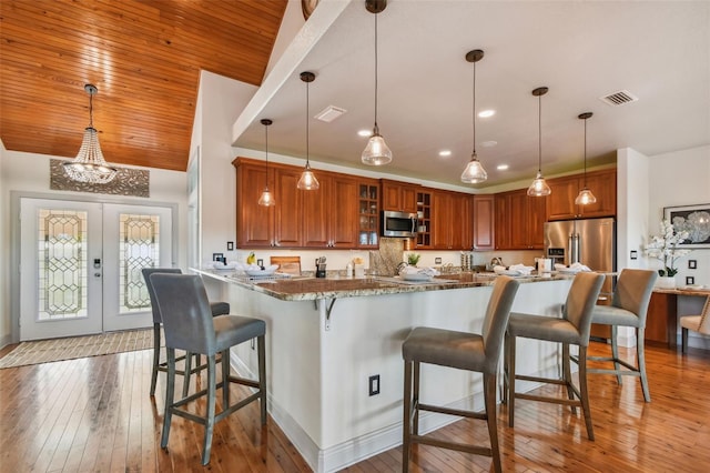 kitchen with light stone countertops, appliances with stainless steel finishes, pendant lighting, and a kitchen breakfast bar