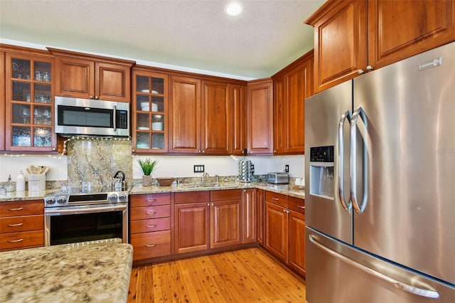 kitchen with light stone countertops, sink, stainless steel appliances, tasteful backsplash, and light hardwood / wood-style floors