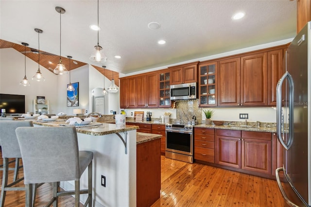 kitchen featuring pendant lighting, high vaulted ceiling, appliances with stainless steel finishes, light hardwood / wood-style floors, and light stone counters