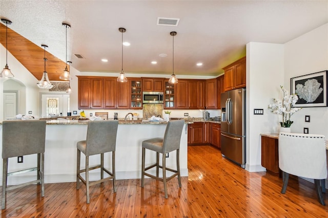 kitchen featuring light stone countertops, pendant lighting, stainless steel appliances, and light hardwood / wood-style flooring