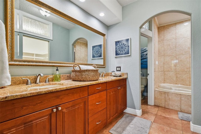 bathroom with tile patterned flooring, vanity, a relaxing tiled tub, and toilet