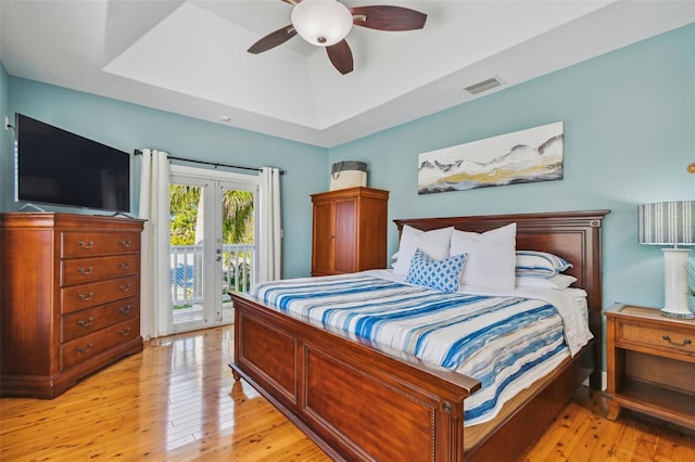 bedroom featuring access to exterior, light hardwood / wood-style floors, a raised ceiling, and ceiling fan