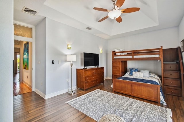 bedroom with a tray ceiling, ceiling fan, and dark wood-type flooring