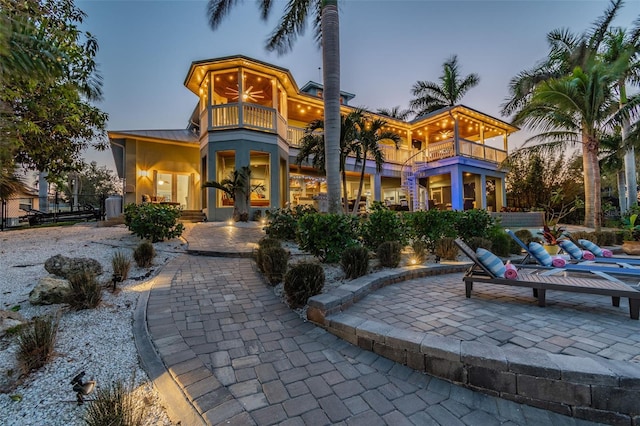 back house at dusk featuring a patio area, ceiling fan, and a balcony