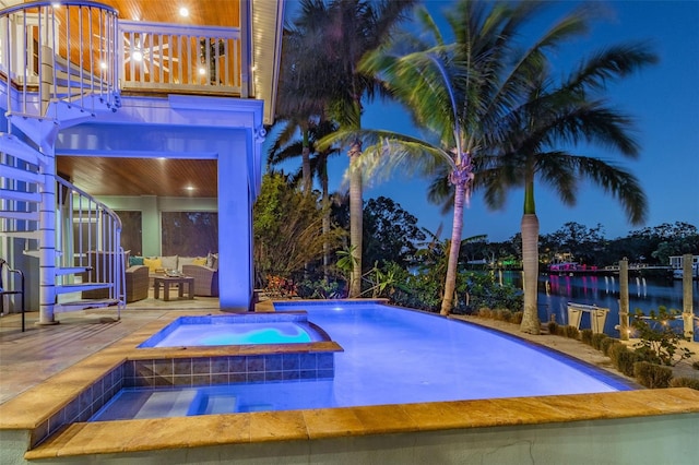 pool at night featuring an outdoor living space, a water view, an in ground hot tub, and a patio