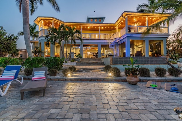 back house at dusk featuring a patio area, ceiling fan, and a balcony