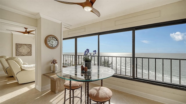 tiled dining room with a water view, ceiling fan, ornamental molding, and a view of the beach