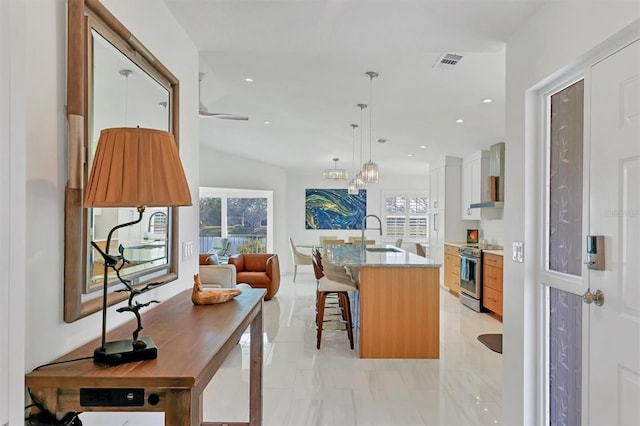 kitchen with electric range, sink, a kitchen breakfast bar, an island with sink, and white cabinets