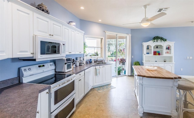 kitchen featuring butcher block counters, white cabinets, a sink, white appliances, and a kitchen breakfast bar