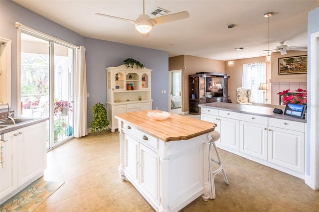 kitchen with white cabinetry, a kitchen island, a sink, ceiling fan, and butcher block countertops