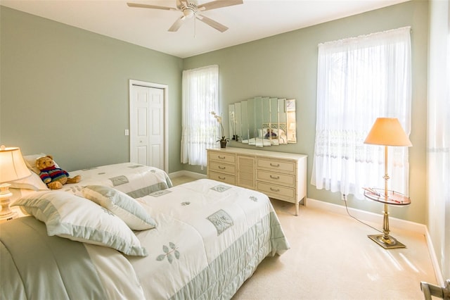 bedroom featuring baseboards, a closet, a ceiling fan, and light colored carpet