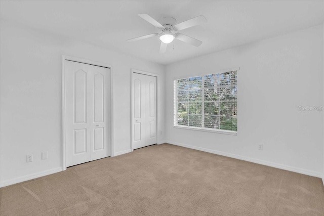 unfurnished bedroom featuring ceiling fan, light colored carpet, and multiple closets