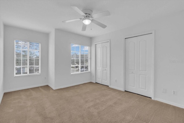 unfurnished bedroom with light carpet, two closets, multiple windows, and ceiling fan