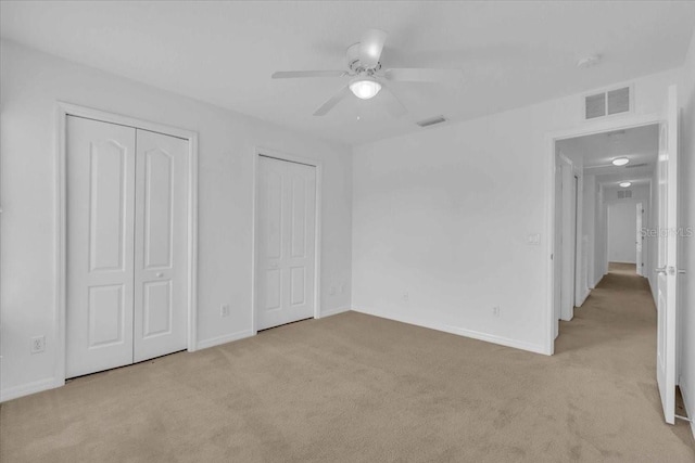 unfurnished bedroom with ceiling fan, light colored carpet, and two closets