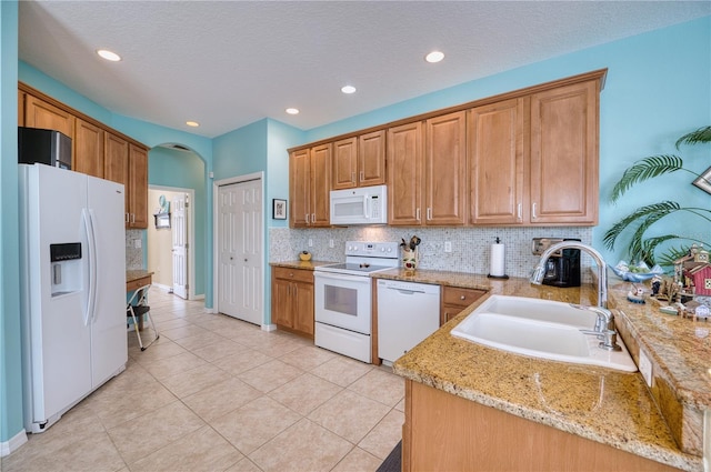 kitchen with kitchen peninsula, light stone counters, a textured ceiling, white appliances, and sink