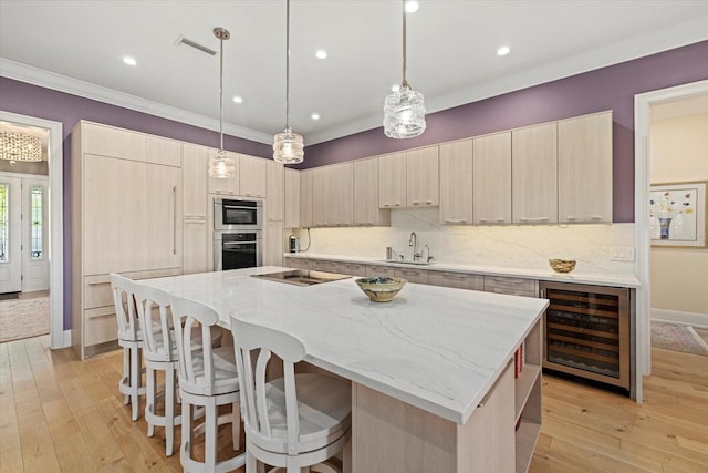 kitchen with stainless steel oven, beverage cooler, light brown cabinets, decorative light fixtures, and a kitchen island