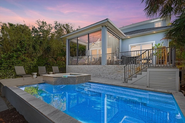 pool at dusk with a sunroom, an in ground hot tub, and a patio area