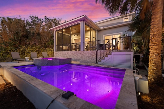 pool at dusk with an in ground hot tub, ceiling fan, a patio area, and a sunroom