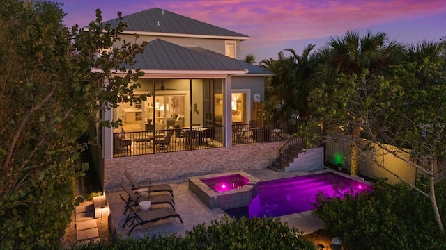 back house at dusk featuring a swimming pool with hot tub, ceiling fan, and a patio area