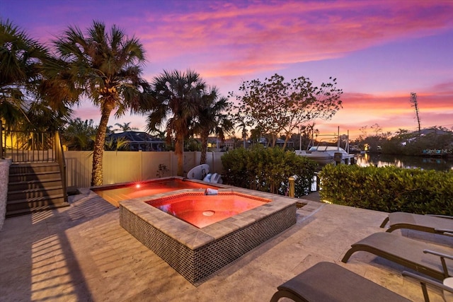 patio terrace at dusk with a water view and an in ground hot tub