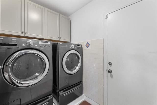 laundry area with cabinets, tile walls, and washing machine and clothes dryer