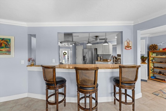 kitchen featuring crown molding, stainless steel refrigerator with ice dispenser, decorative light fixtures, a kitchen bar, and kitchen peninsula