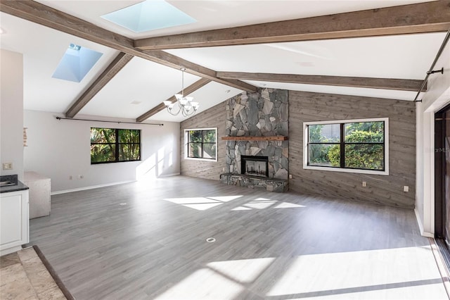 unfurnished living room with lofted ceiling with skylight, a chandelier, a stone fireplace, and light hardwood / wood-style flooring