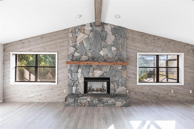 unfurnished living room with vaulted ceiling with beams, wood walls, and a stone fireplace