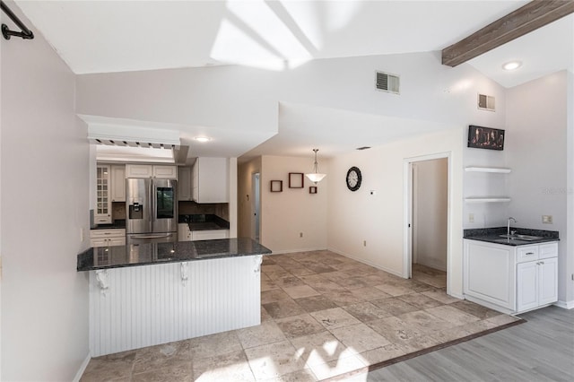 kitchen with white cabinetry, kitchen peninsula, stainless steel fridge, sink, and vaulted ceiling with beams