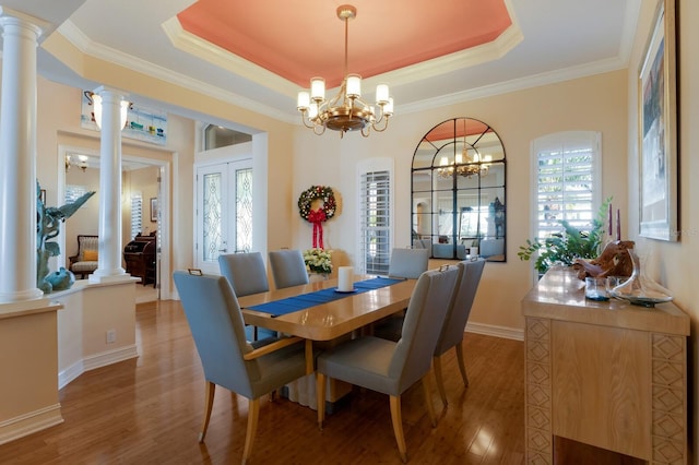 dining area with a tray ceiling, ornate columns, a wealth of natural light, and hardwood / wood-style floors